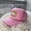 Thumbnail: Detailed view of pink trucker hat with Lucky or Not embroidered patch and gold trim