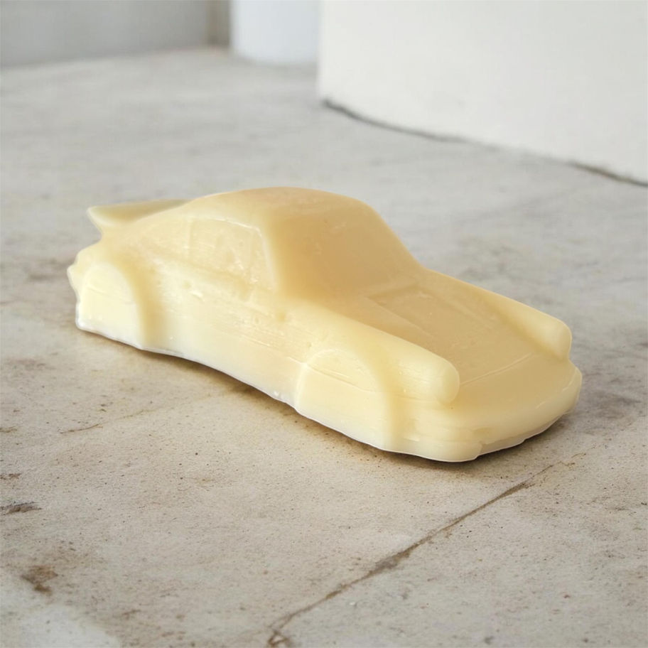 Handmade ivory porsche-inspired sculptural candle poured in soy pillar wax and displayed on a light stone surface