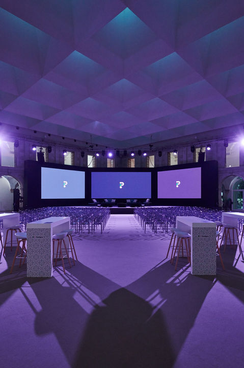 Corporate event in a brightly lit room – Conference room with purple lighting, tables arranged in rows and three large screens with question marks.