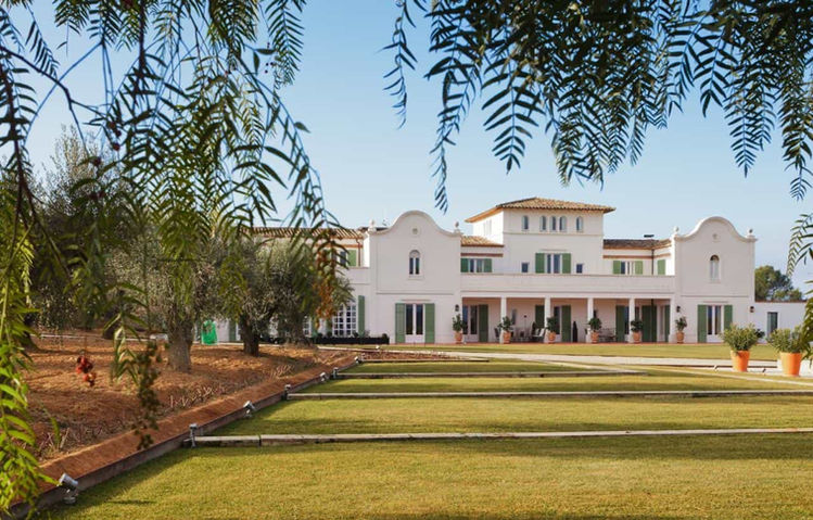 Masía blanca rodeada de jardines y naturaleza: Impresionante finca con arquitectura tradicional, césped bien cuidado y árboles en un entorno rural.
