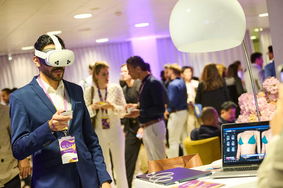 Asistente con gafas de realidad virtual explorando un stand tecnológico – Innovación y experiencias inmersivas en evento de networking.