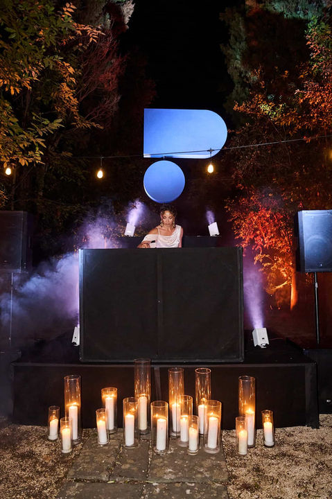 Evento al aire libre con decoración minimalista, luces cálidas y un ambiente rodeado de vegetación y niebla.