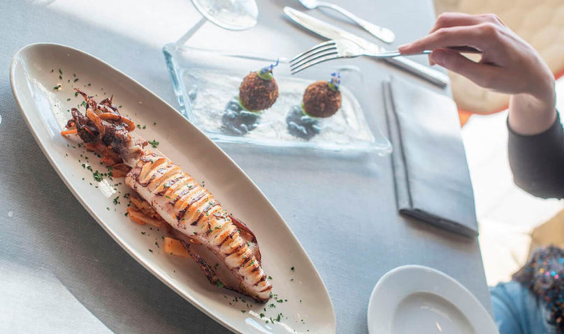 Plato gourmet con mariscos y aperitivos servidos sobre mantel blanco – alta cocina mediterránea en presentación elegante.