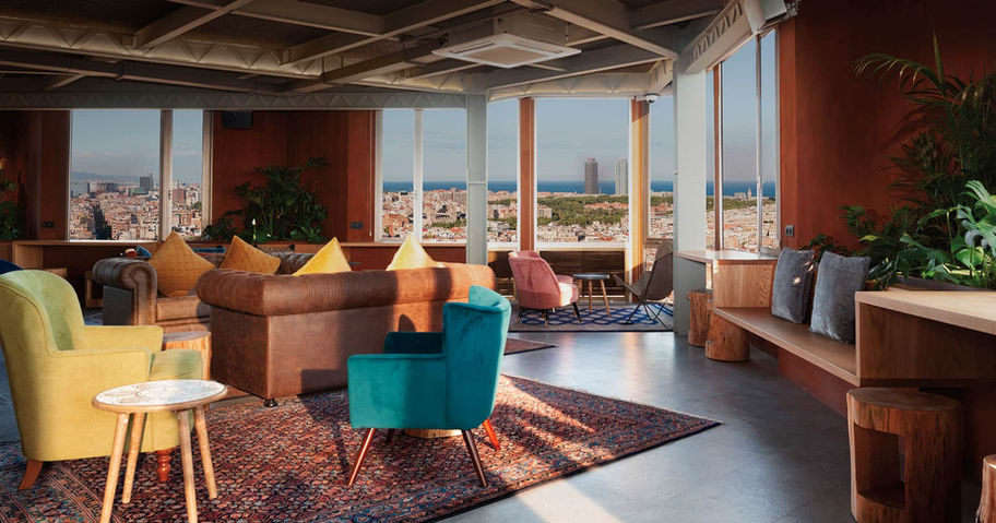 Sala de estar con vistas a la ciudad: Espacio amplio con sofás de colores, alfombra y decoración moderna en un entorno con grandes ventanales.
