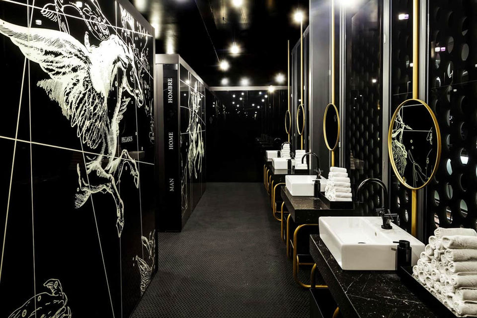 Baño de restaurante con paredes negras, arte mural y lavabos modernos – aseo de diseño sofisticado en blanco y negro.