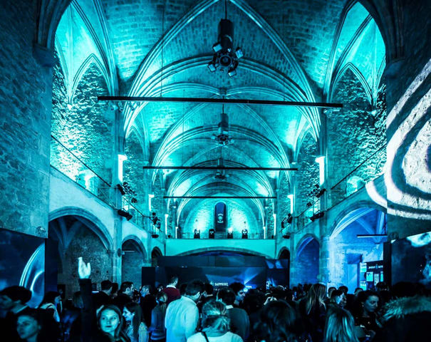 Fiesta en iglesia antigua con luces azules: Multitud disfrutando de un evento en un espacio con arcos góticos.