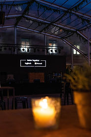 Evento corporativo nocturno en ISE Barcelona – Escenario al aire libre con un letrero "Better Together Logitech & Microsoft", bajo una carpa iluminada con velas y detalles decorativos naturales.