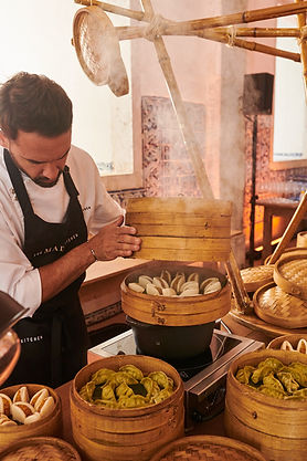Chef preparing steamed baos and dumplings in an open kitchen with bamboo – Chef serving Asian food in bamboo baskets at a food event.