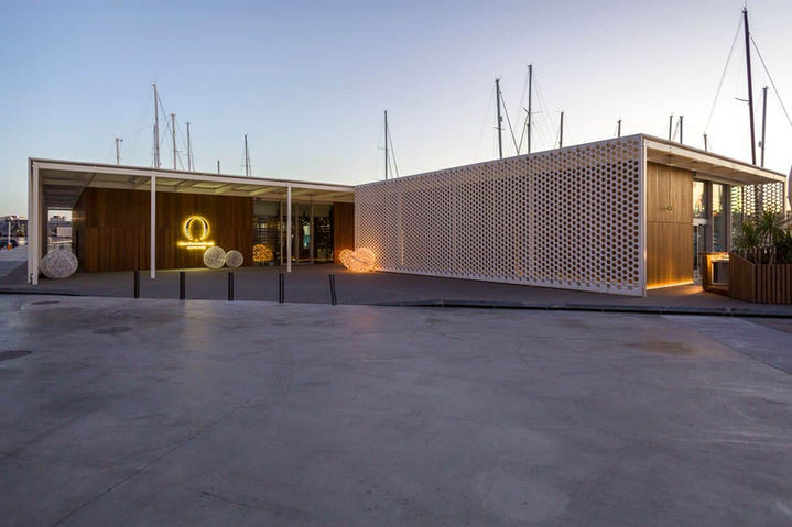 Entrada del restaurante al atardecer con arquitectura moderna y logo iluminado – fachada de restaurante contemporáneo.