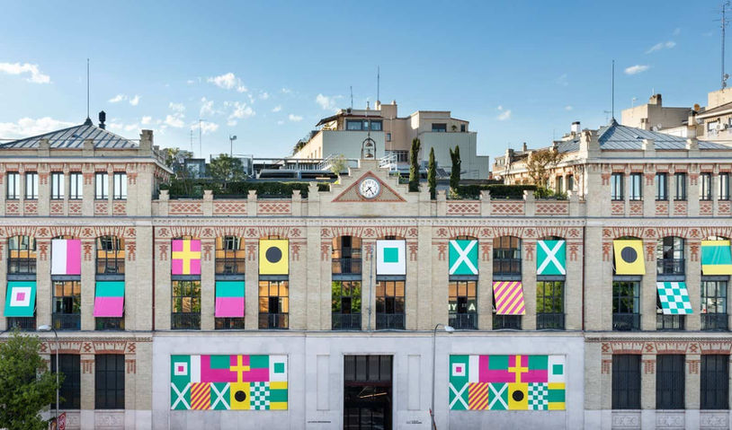 Fachada con ventanas decoradas con colores vibrantes y símbolos gráficos, reflejando el carácter creativo e innovador del espacio.
