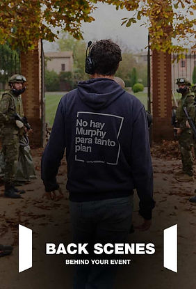 Persona de espaldas, vistiendo una sudadera, caminando en un entorno exterior otoñal con hojas caídas, mientras en el fondo aparecen personas con equipo táctico en actitud relajada.