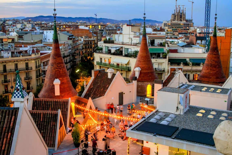 Terraza iluminada de la Casa de les Punxes al atardecer: Espacio al aire libre con luces cálidas, gente disfrutando y torres modernistas de fondo.