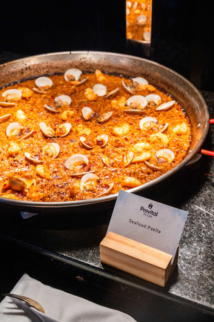 Paella de mariscos servida en una gran sartén con cartel de presentación – Cocina española en evento gastronómico de lujo.