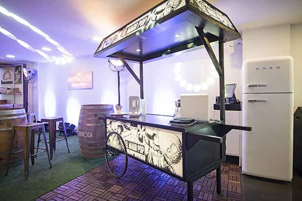 Puesto de comida en un evento cultural – Carrito de estilo vintage ofreciendo snacks y bebidas en un espacio de entretenimiento.