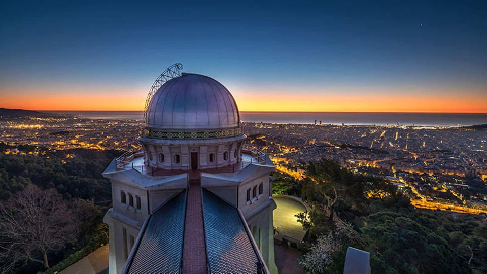 Observatorio Fabra al atardecer, con la cúpula astronómica resaltando sobre la ciudad iluminada.