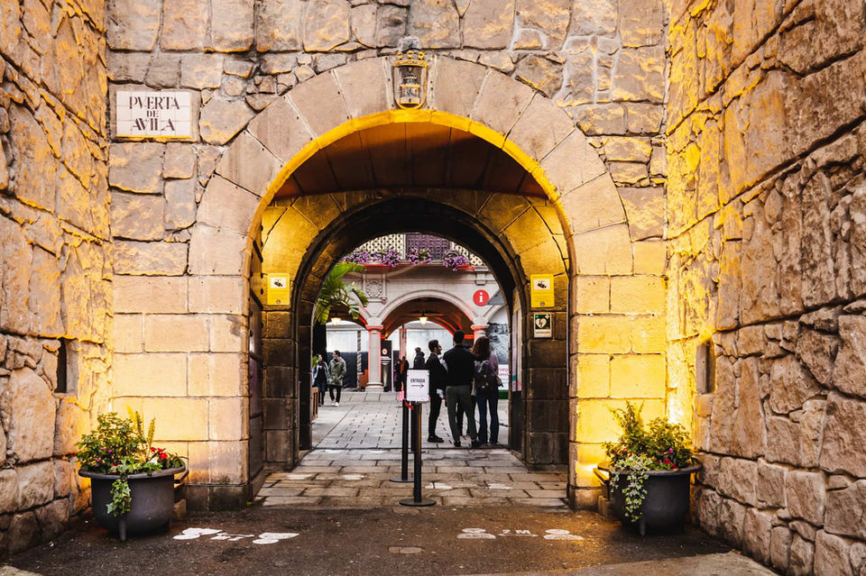 Arco de piedra en un recinto histórico – Entrada a un pasillo con suelo de piedra, muros antiguos y vista a un patio interior.
