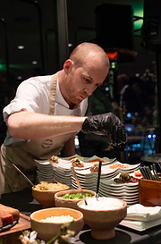 Chef preparando platos gourmet en ISE Barcelona – Cocinero con guantes negros y delantal detallando cuidadosamente platos de alta cocina en un evento exclusivo con ambiente sofisticado.