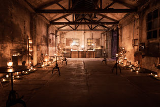 Industrial space with warm lighting, candles on the floor and minimalist furniture, creating a rustic and cozy atmosphere for an event.