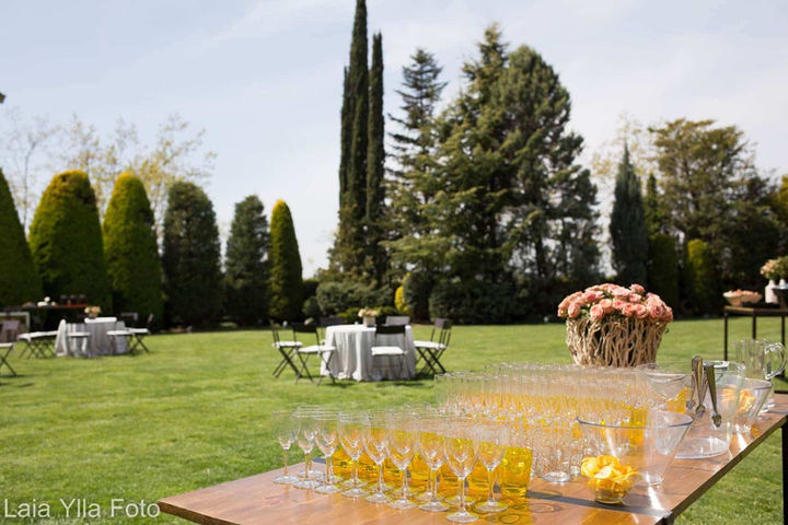 Mesa con copas de vino en jardín con árboles y césped: Montaje elegante para cóctel en un entorno natural.
