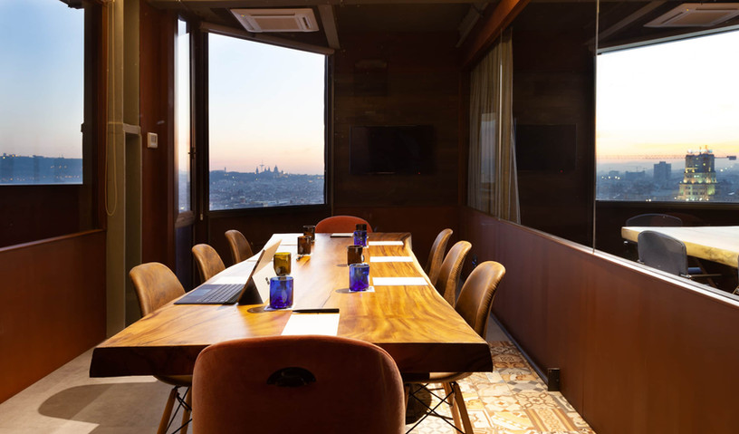 Sala de reuniones con decoración cálida y vistas panorámicas: Espacio de trabajo con mesa de madera, sillas cómodas y luz natural desde grandes ventanales.
