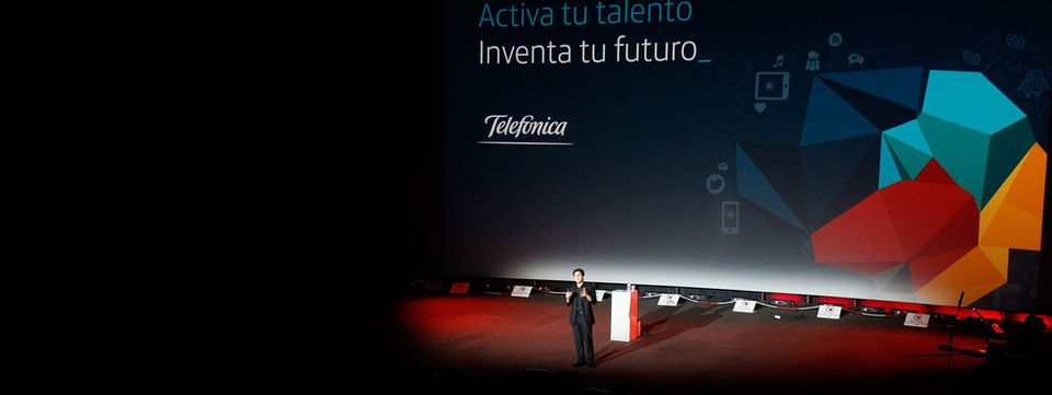 Escenario con una pantalla grande mostrando "Activa tu talento, inventa tu futuro - Telefónica", en un evento de desarrollo profesional y networking.
