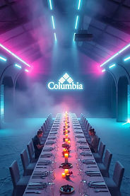 Gala dinner with a long table illuminated in neon pink and blue tones, with the "Columbia" logo projected onto a modern space filled with smoke and futuristic lights.