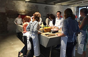 Cooking class with participants wearing aprons and preparing ingredients – Group of people in a cooking workshop, gathered around a counter with food and cooking utensils.