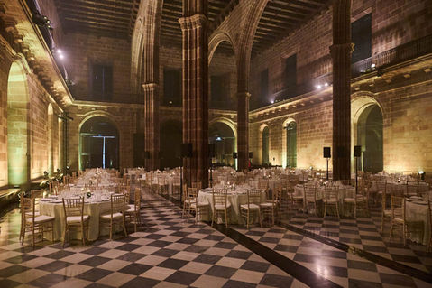 Banquete en un espacio industrial con decoración clásica, suelo de tablero blanco y negro, y sillas doradas.