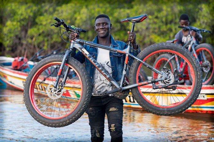 Joven sosteniendo una bicicleta con orgullo – Hombre sonriendo mientras levanta una bicicleta de montaña en un entorno natural.