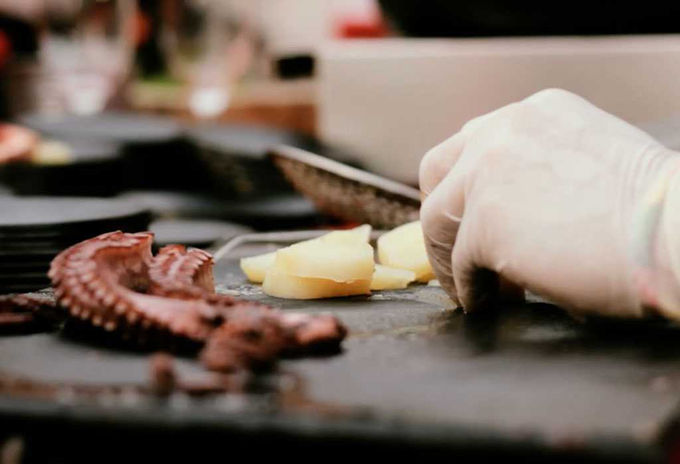 Pulpo a la parrilla con patatas siendo preparado en una cocina gourmet – Plato de mariscos cocinado a la brasa con ingredientes frescos.