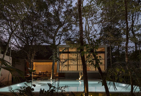 Outdoor pool surrounded by trees, with warm lighting and outdoor furniture to relax in a peaceful atmosphere.