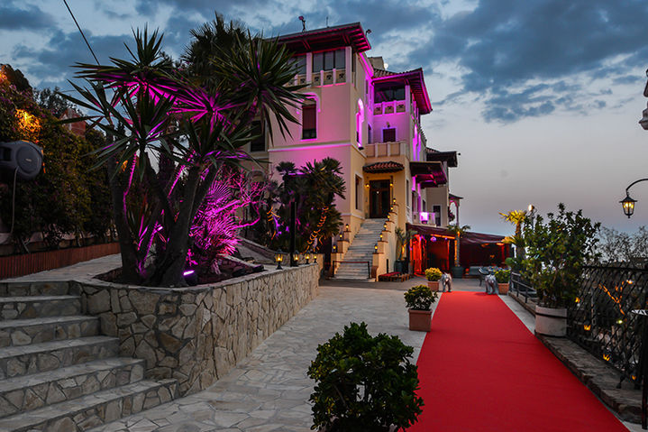 Entrada con alfombra roja a un palacio exclusivo, con palmeras y luces decorativas, ideal para eventos VIP.