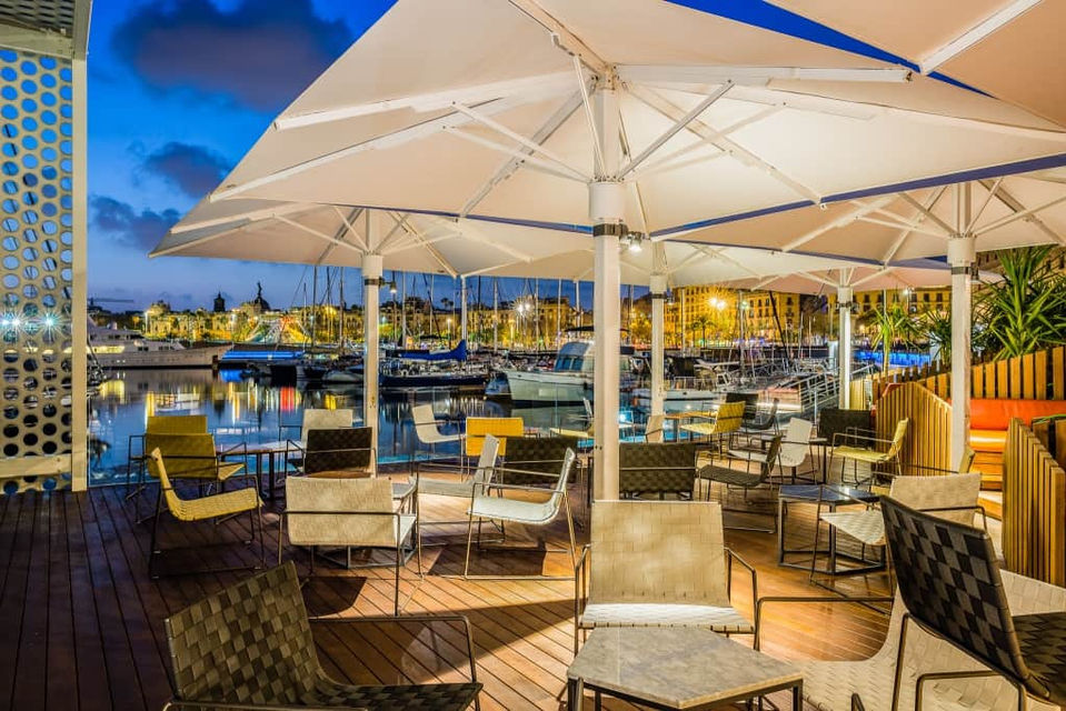 Terraza junto al agua con sombrillas blancas y vistas a embarcaciones – restaurante costero con ambiente náutico.