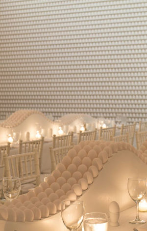 Event decorated in white tones, with long tables, classic style chairs and a decorative background with curved patterns.