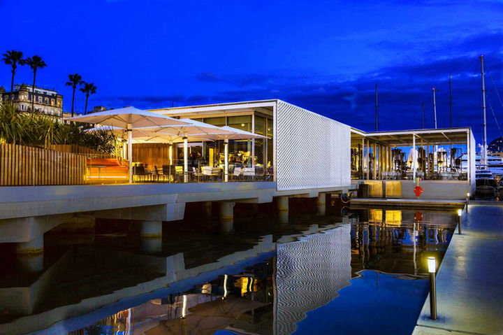 Vista nocturna del restaurante con luces cálidas reflejadas en el agua, diseño minimalista – experiencia gastronómica frente al mar.