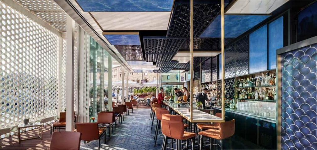 Restaurante moderno con techo geométrico, sillas naranjas y paredes de cristal – ambiente chic para almuerzos elegantes.
