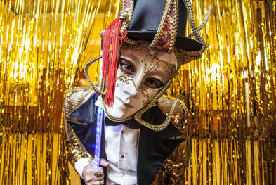 Artista con máscara dorada y vestuario de circo veneciano en fiesta de empresa exclusiva, en una atmósfera misteriosa.
