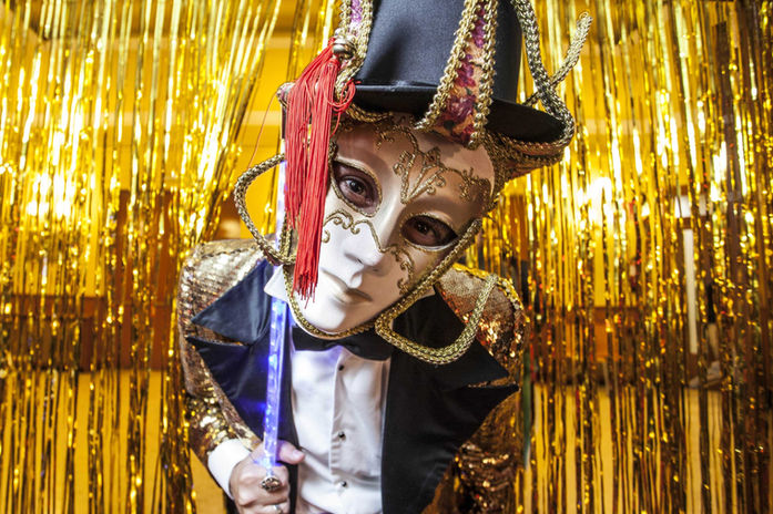Persona con máscara veneciana y traje dorado en un evento temático – Estética de carnaval con vestuario elegante y teatral.