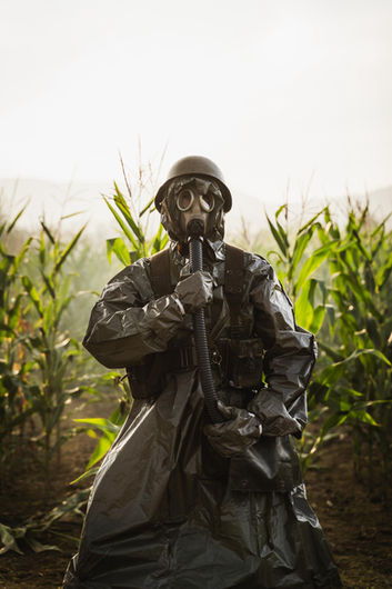 Persona con traje militar y máscara de gas en un campo de maíz, evocando una misión de supervivencia o un escape postapocalíptico.
