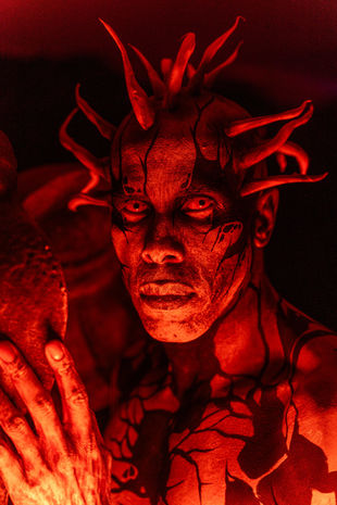 Hombre con pintura roja y cuernos en un evento con iluminación intensa.