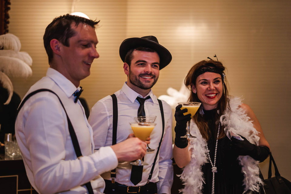 Grupo de invitados brindando con cócteles, vestidos con atuendos de los años 20.