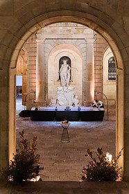 Evento exclusivo en Integrated Systems Europe (ISE) Barcelona en un entorno histórico – Vista a través de un arco de piedra hacia un elegante espacio con una estatua iluminada, decoración clásica y una mesa de cócteles en el centro.