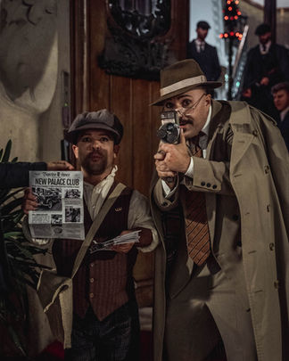 Hombres vestidos de detectives con gabardinas en fiesta de empresa tipo speakeasy, interpretando un juego de rol.