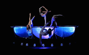 Acróbatas realizando una rutina artística sobre una plataforma iluminada, combinando fuerza y equilibrio.