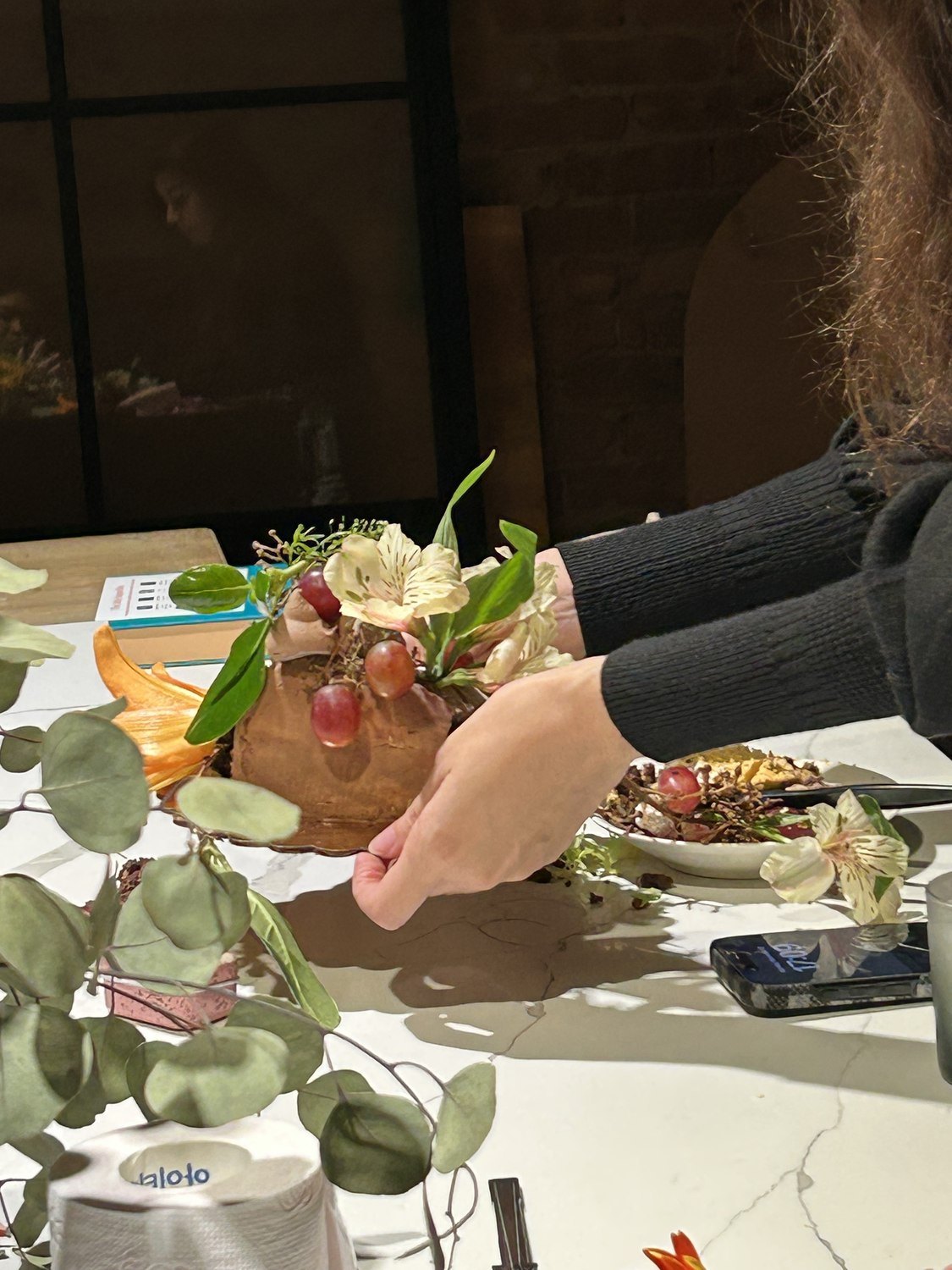 Hands arranging flowers and objects around a table at De Duallè.