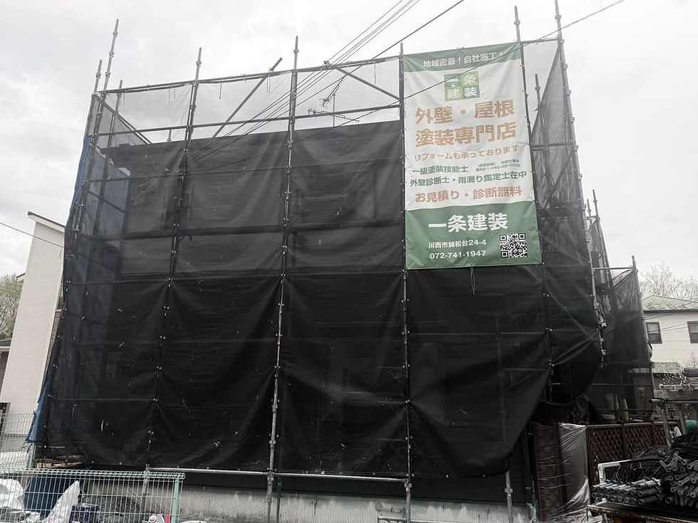 塗装工事中の足場が立っている川西市の住宅。一条建装の現場シート（看板）が足場に貼ってある。