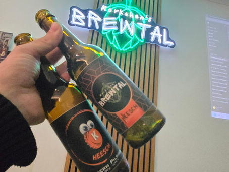 Zwei BrewTal Bierflaschen (HEESCH Modern Pilsner) vor leuchtendem BrewTal Neonlogo an der Wand