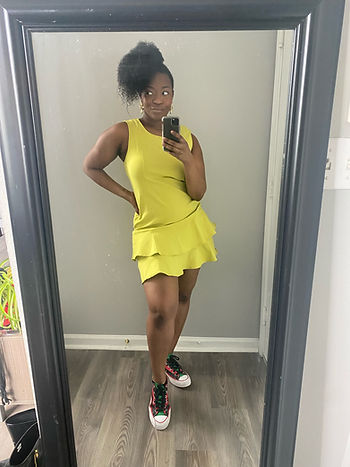 Image is a mirror pic of Teryn with a side curly ponytail and a lime green dress with ruffles and Denim Tears Converse.