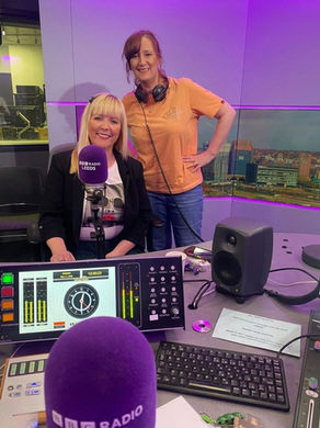 Lisa Norfolk in the BBC Radio Leeds studio during a radio interview, standing beside the presenter with headphones on and broadcasting equipment, microphones and studio screens visible.