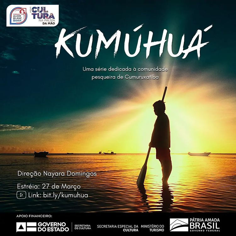 Card promocional do documentário Kumúhuá. A imagem de fundo é uma fotografia tirada contra à luz do sol, retrata uma pessoa em pé, de perfil para a câmera e de frente para o mar, com os pés à beira da água e segurando grande remo, maior que seu corpo e paralelo a este. É possível ver ao fundo alguns barcos e canoas. As cores predominantes são um azul marinho escuro do céu, um amarelo brilhante vindo da luz do sol e tons mais escuros de todos os objetos capturados pela fotografia. O card anuncia: “Aldir Blanc. Prêmio Cultura na Palma da mão. Kumúhuá, uma série dedicada à comunidade pesqueira de Cumuruxatiba. Direção: Nayara Domingos. Estreia: 27 de março. Link: bit.ly/kumuhua. Apoio Financeiro: Governo do Estado; Secretaria de Cultura; Secretaria Especial da Cultura; Ministério do Turismo; Pátria amada Brasil – Governo Federal”